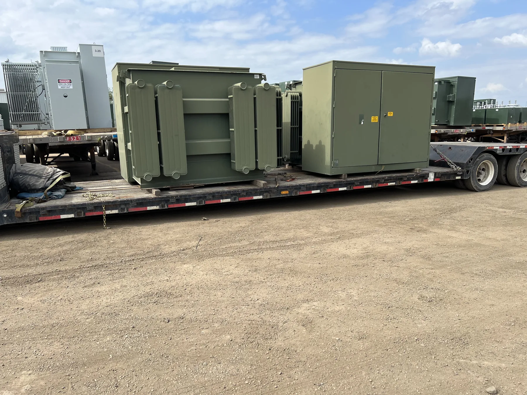 Commercial padmount and radiator-equipped transformers staged on transport trailers